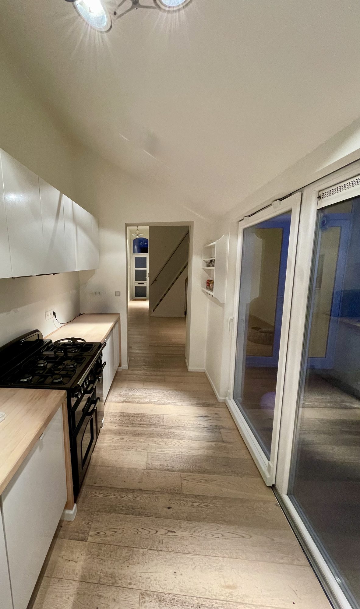 Lange keuken met witte bovenkasten, massieve houten werkbladen, statig blauw Falcon-gasfornuis met dubbele oven en schuifdeuren naar de achterzijde van het huis