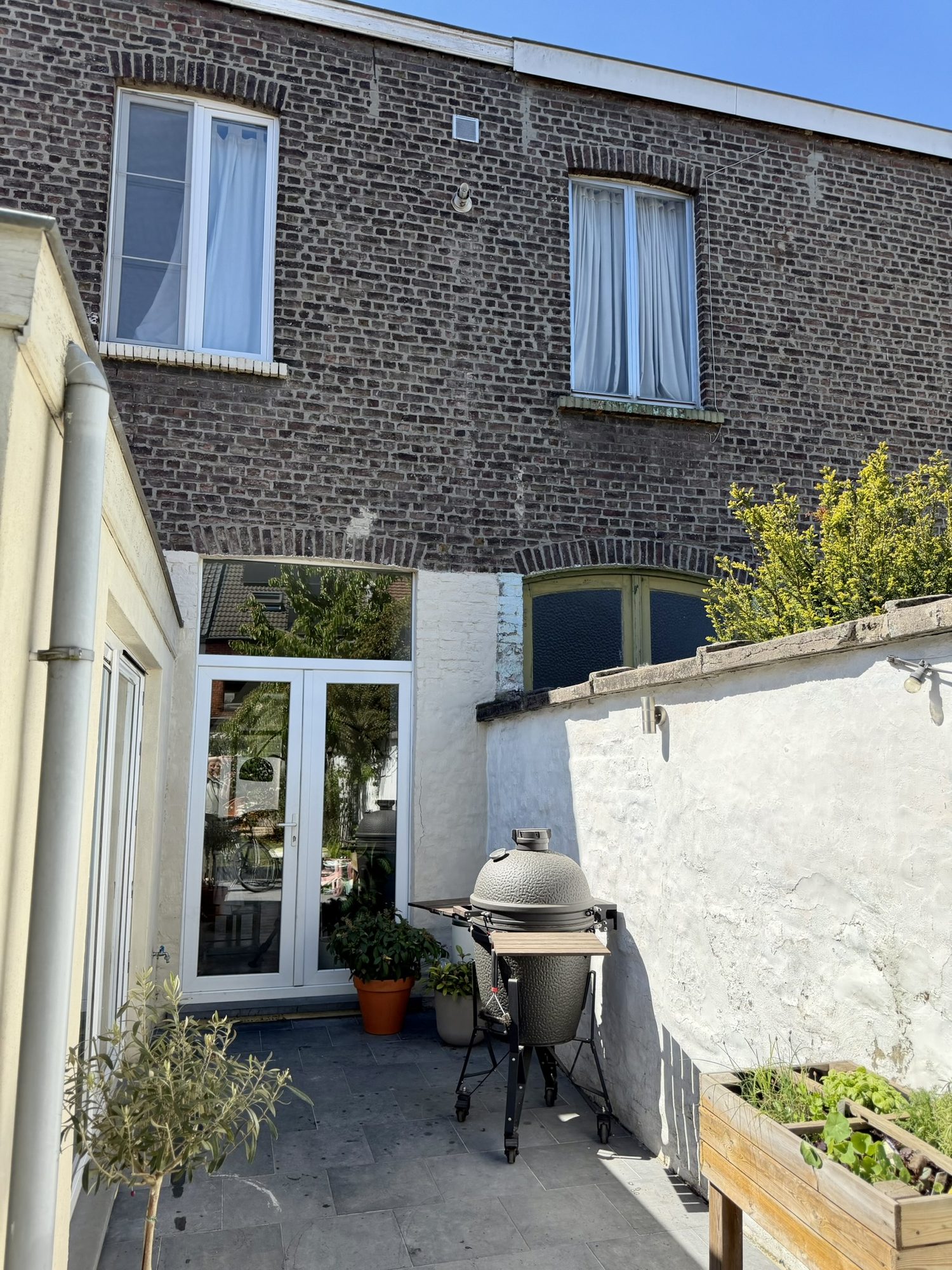 Achterzijde van de woning met natuursteenterras, kamado-grill en openslaande deuren naar de leefruimte